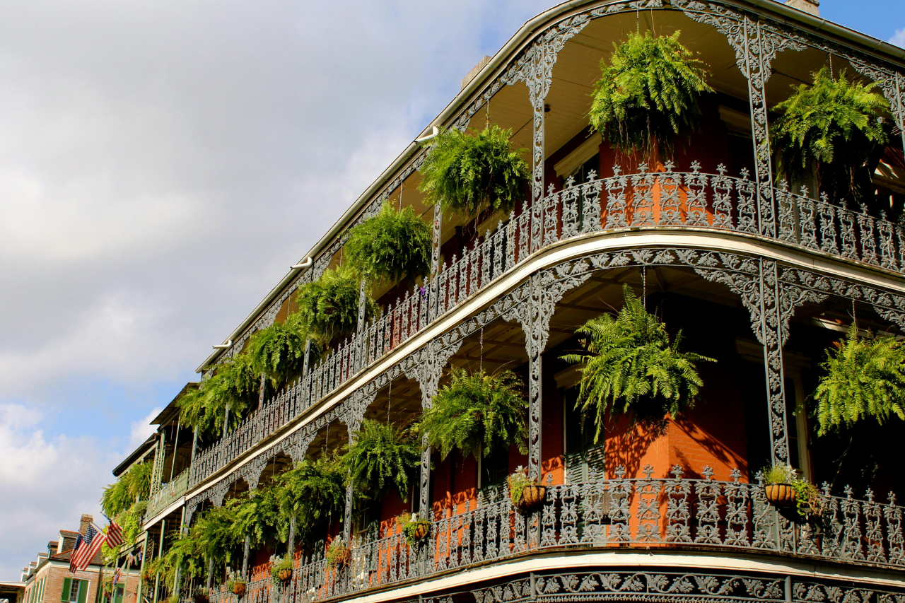 An angled view of a distinctive building in the French Quarter with detailed ironwork and many green hanging ferns.