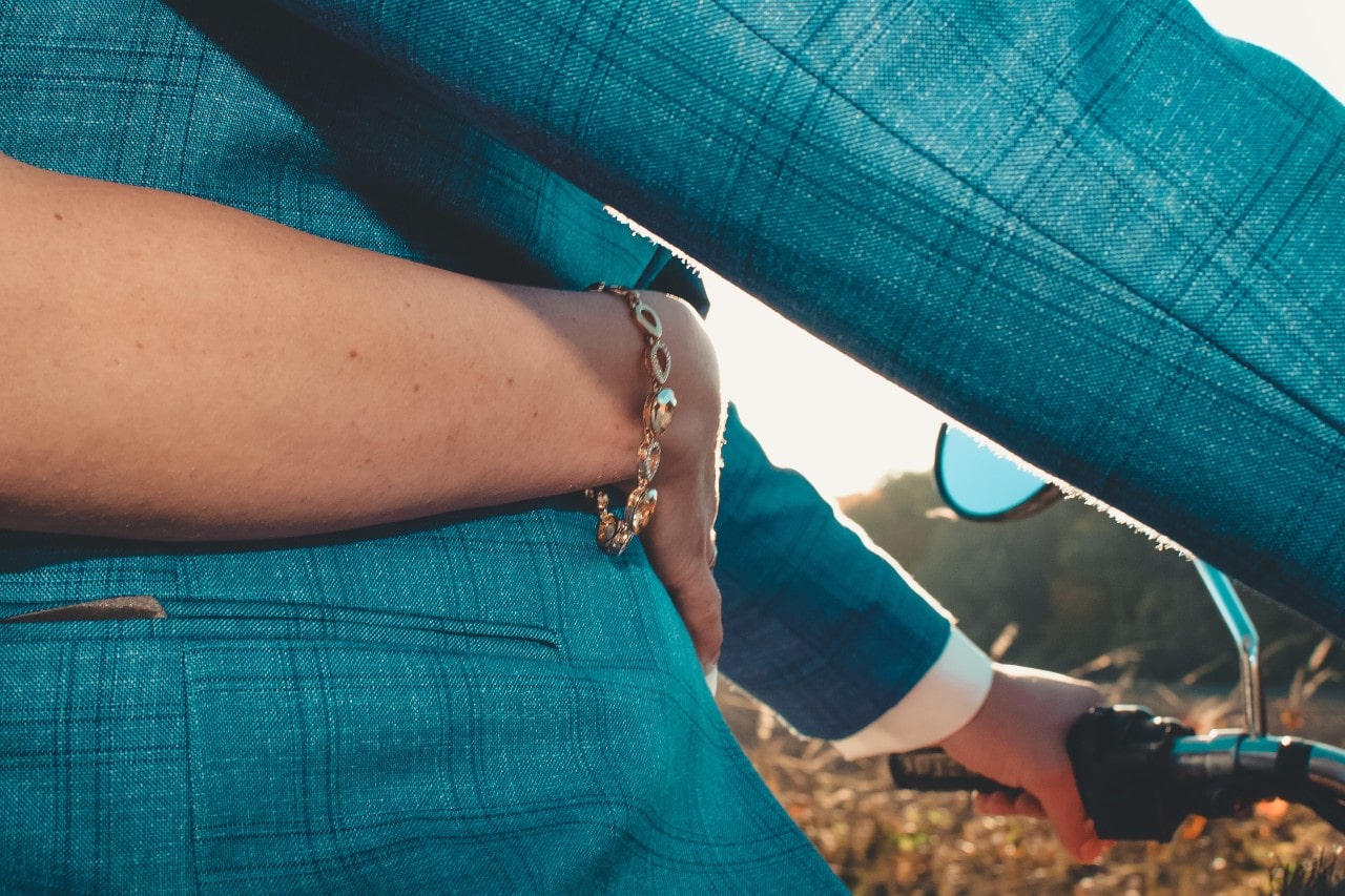 a woman’s bracelets arm wrapped around a person in a blue suit driving a motorcycle