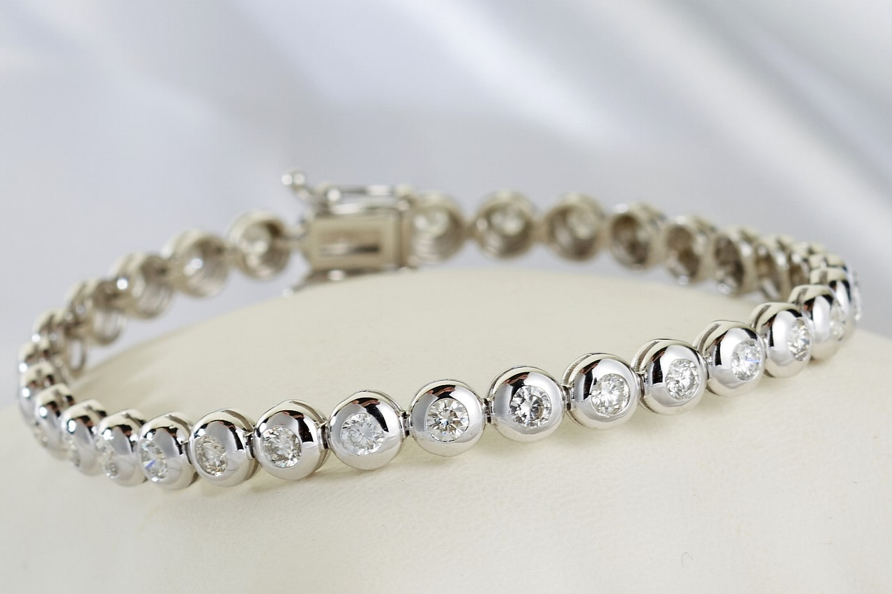 a white gold tennis bracelet featuring bezel set, round cut diamonds