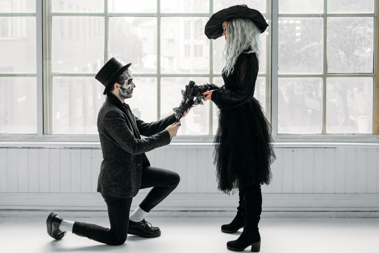 A couple dressed in Halloween costumes poses in a white hall.