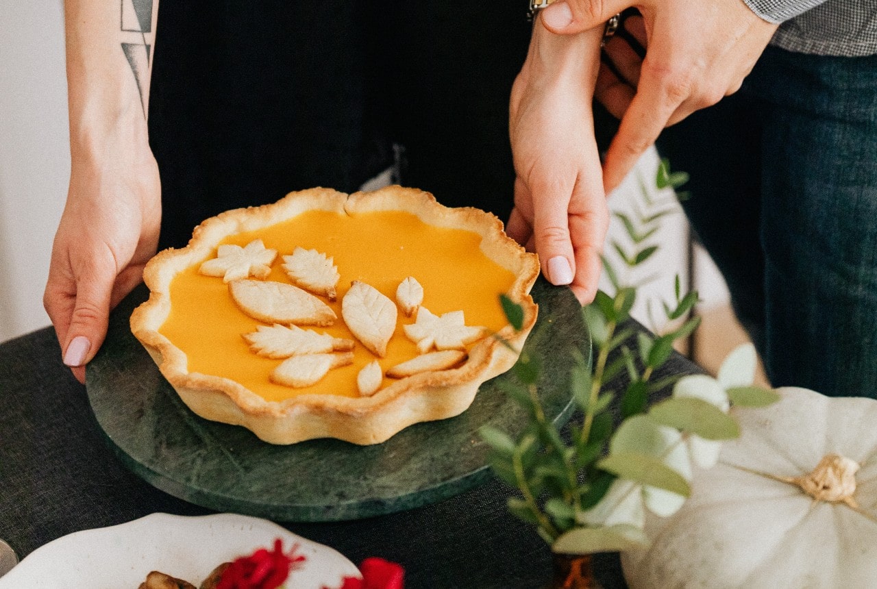 A woman places a pumpkin pie on a table with a man behind her.