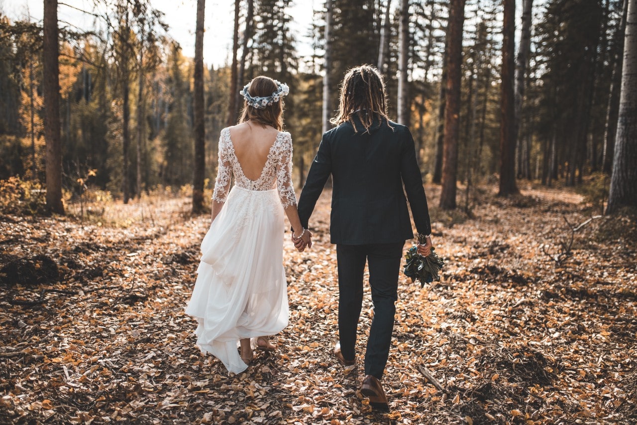 A couple walks in the forest holding hands during the fall.