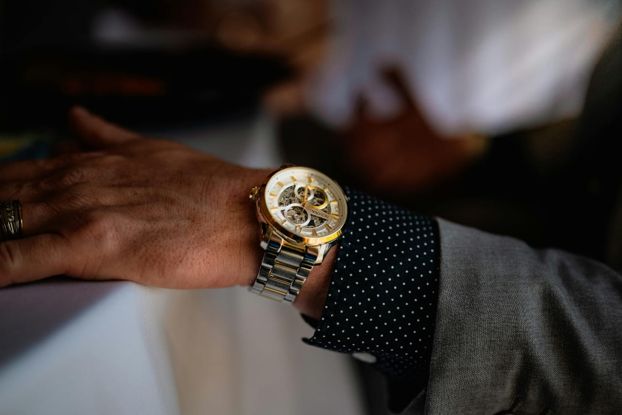 A close up of a gold watch on a person&rsquo;s hand with a gray suit on.