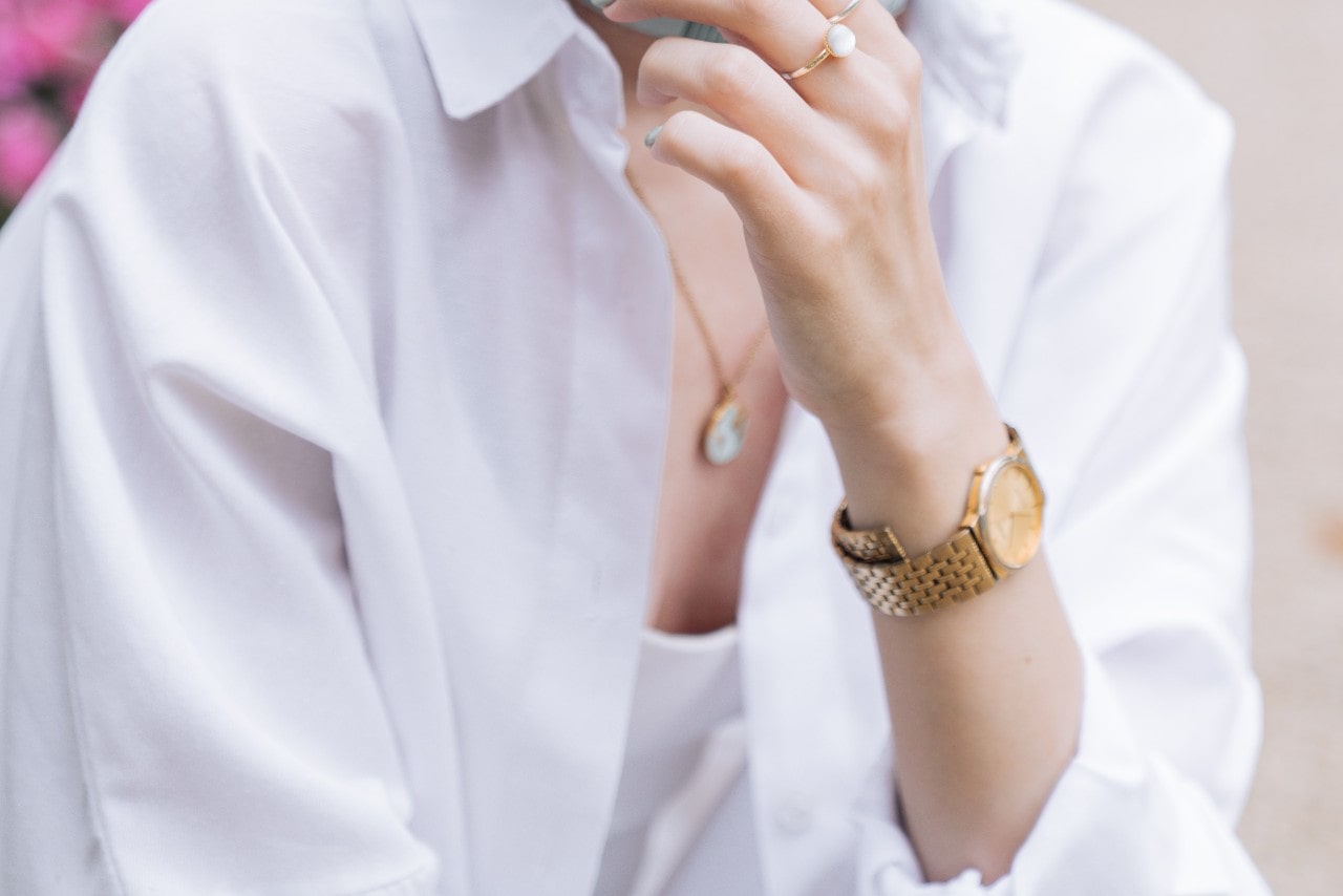 A close up of a woman in a white shirt with yellow gold watch and gold pendant.