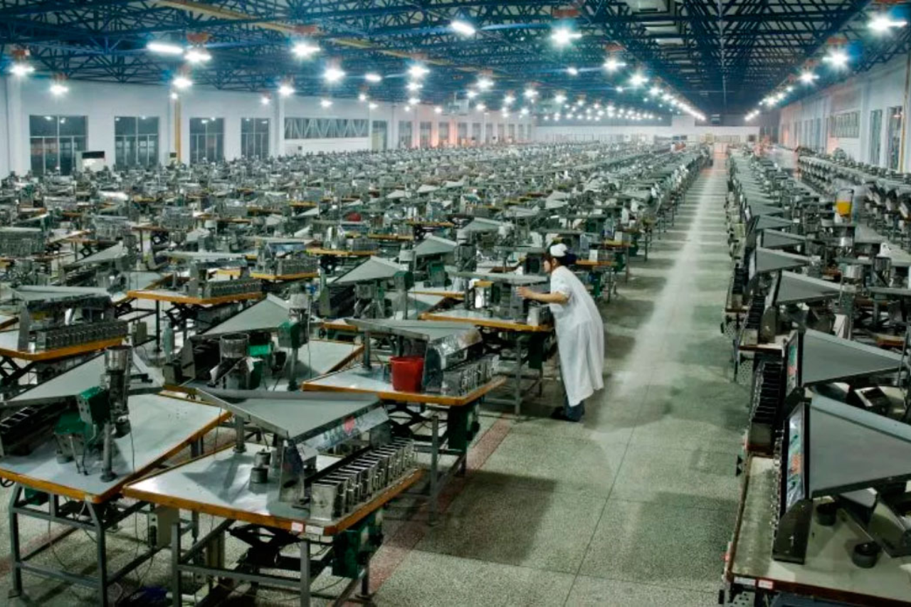 A view of a factory that produces lab-grown diamonds, with many stations of HPHT presses stretching up and down the long room while a single employee checks one of the machines.
