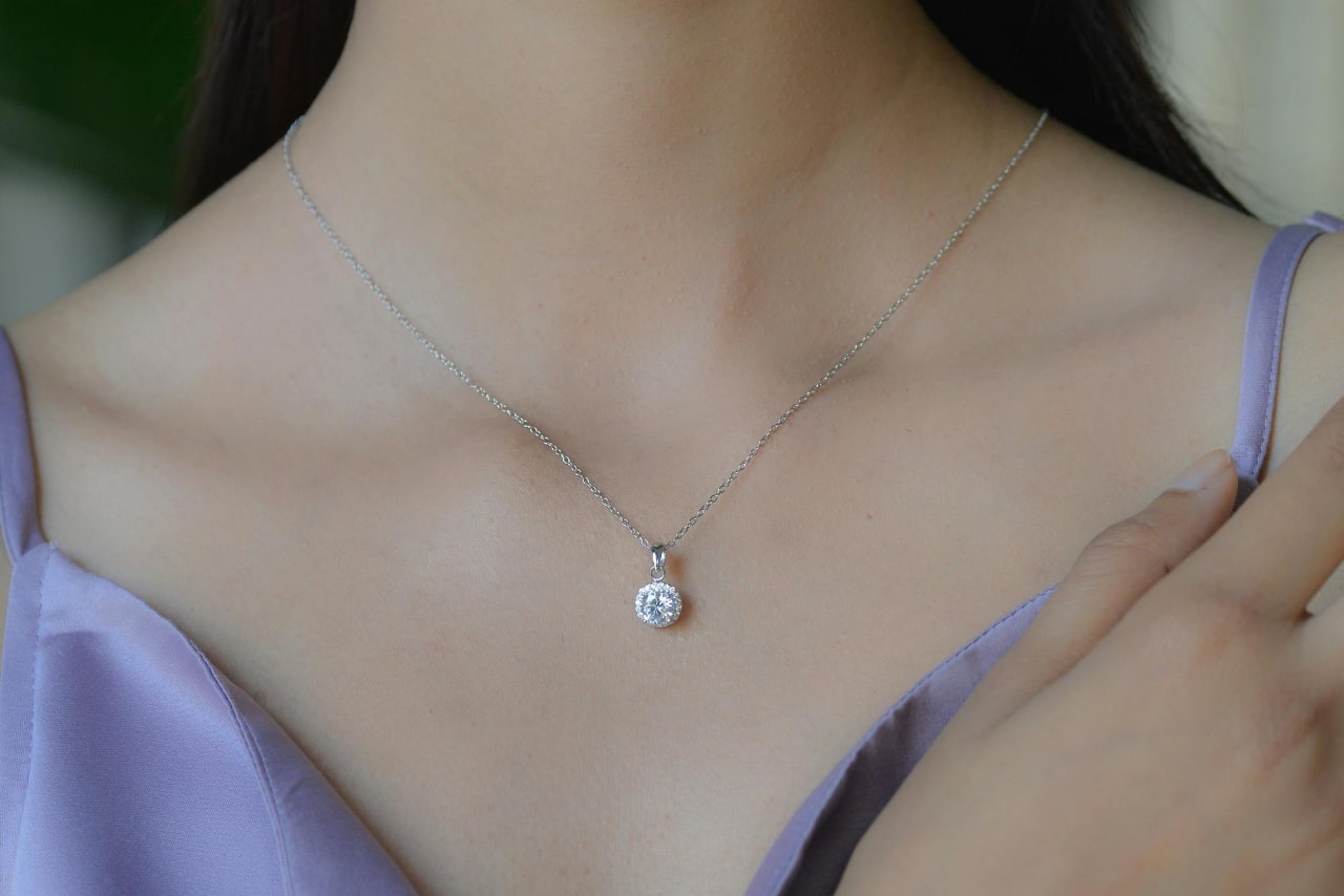 A close-up of a woman wearing a simple lilac dress, with a delicate diamond necklace decorating her decolletage.