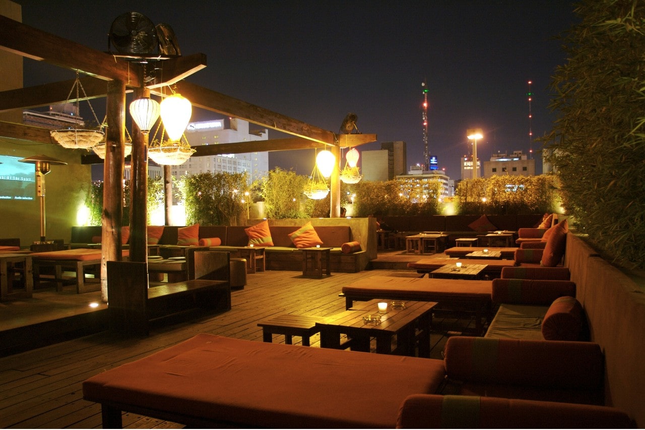 an empty rooftop bar with warm lighting and a city scape in the background