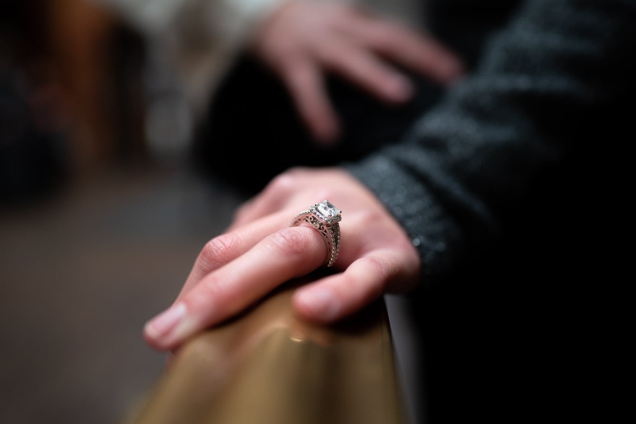 a woman’s hand resting on a bannister, wearing an elaborate diamond engagement ring