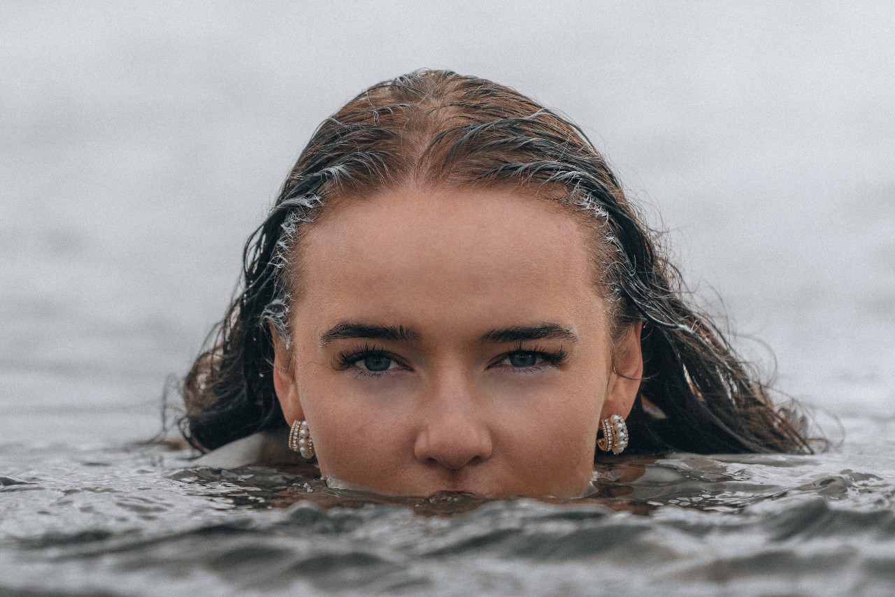 a woman’s face, half-submerged in water and wearing layered hoop earrings