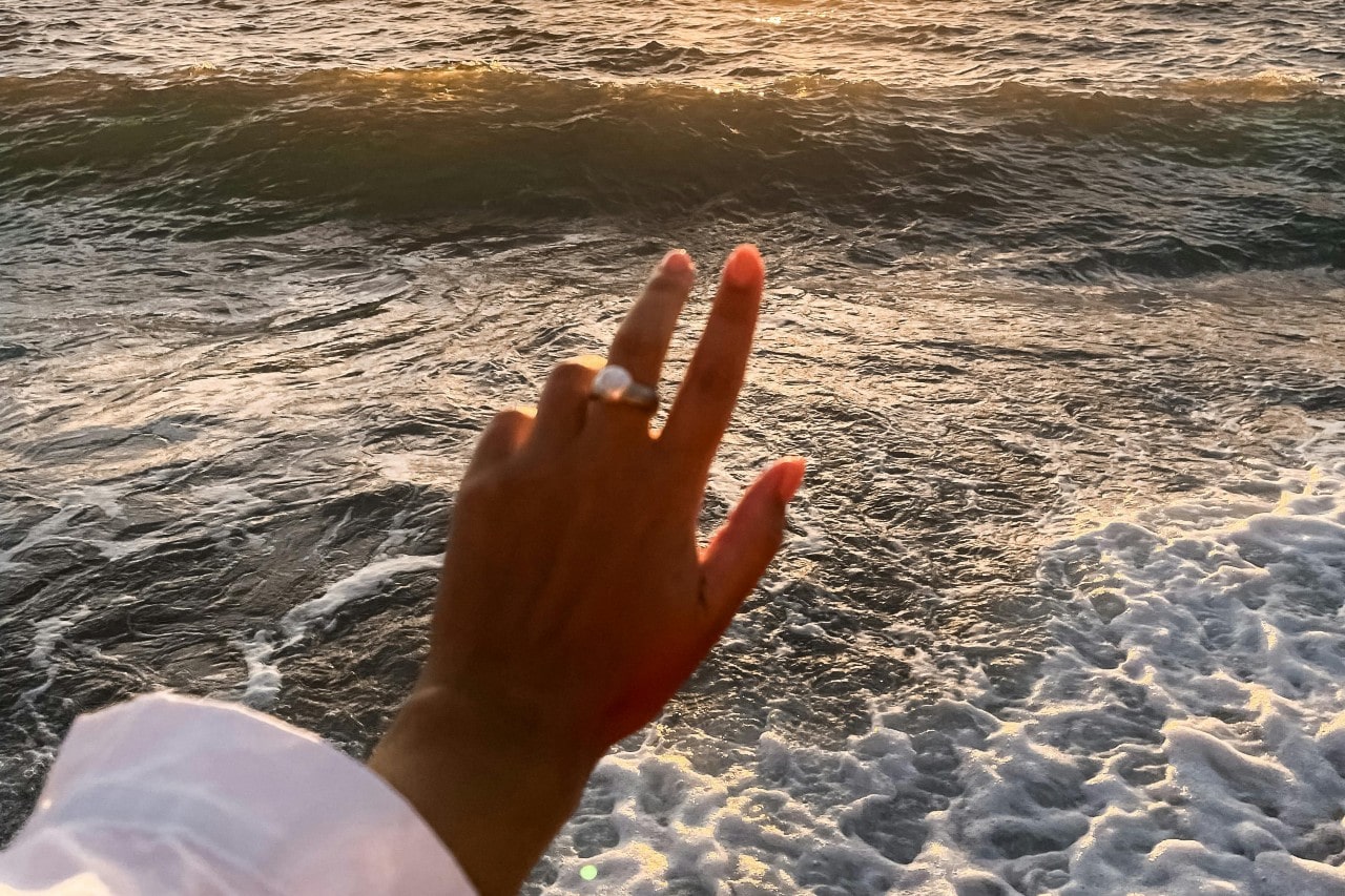 a woman’s hand extended toward the ocean, wearing a large pearl fashion ring