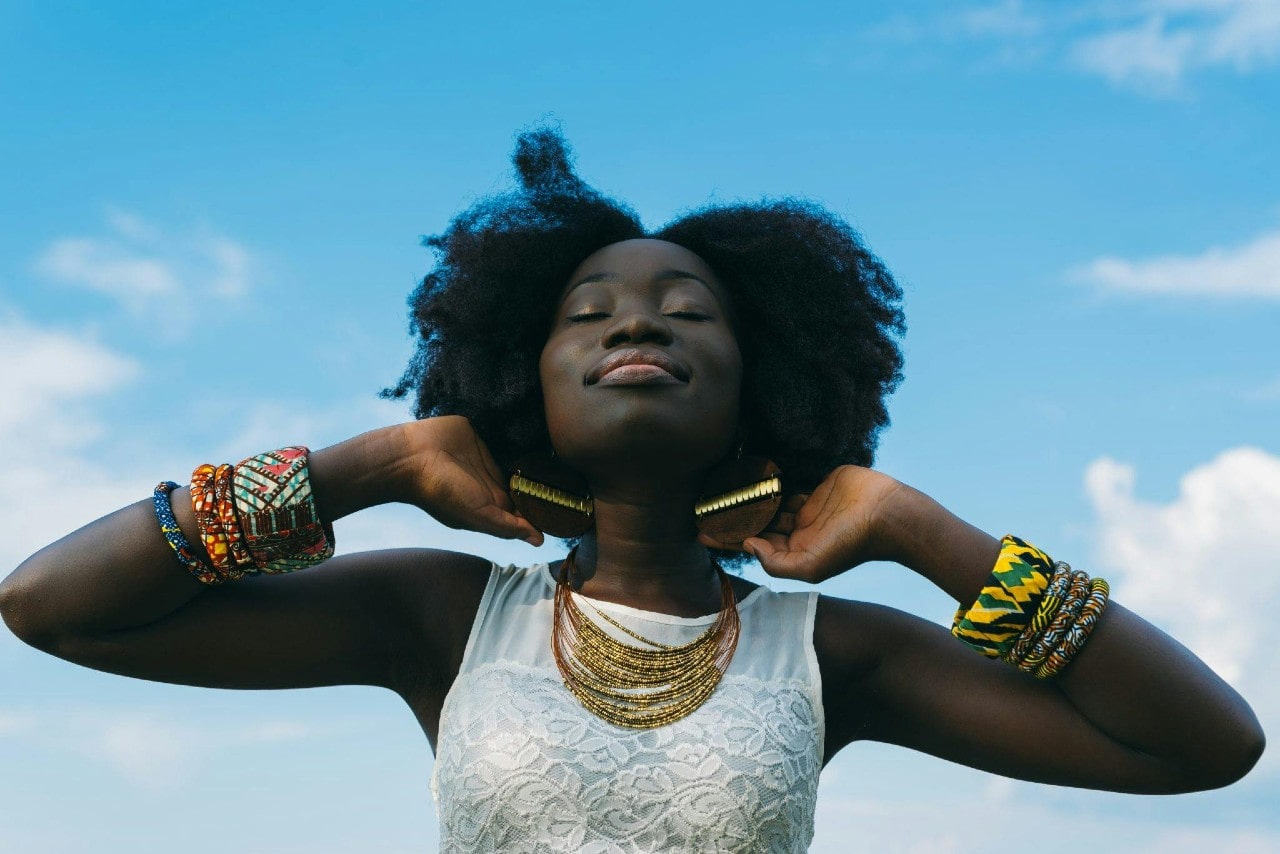 a woman wearing large pieces of colorful gold jewelry and smiling