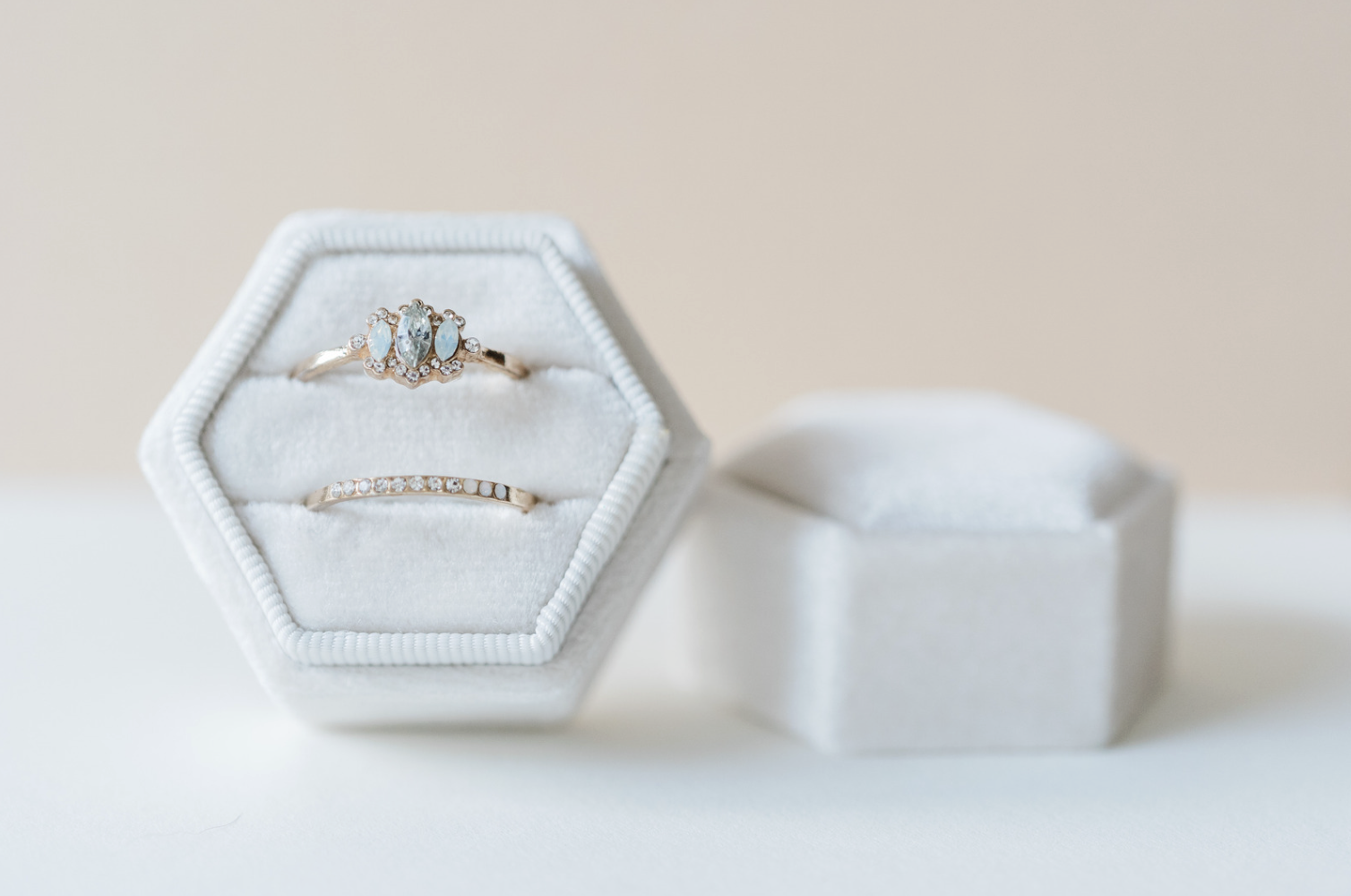 A wedding ring set featuring an opal and diamond cluster ring and a matching pavé band, displayed in a white hexagonal velvet box.