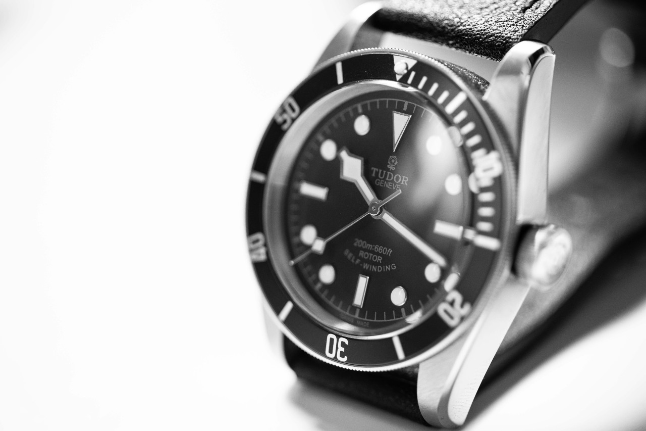 A black TUDOR watch with a leather strap against a white background