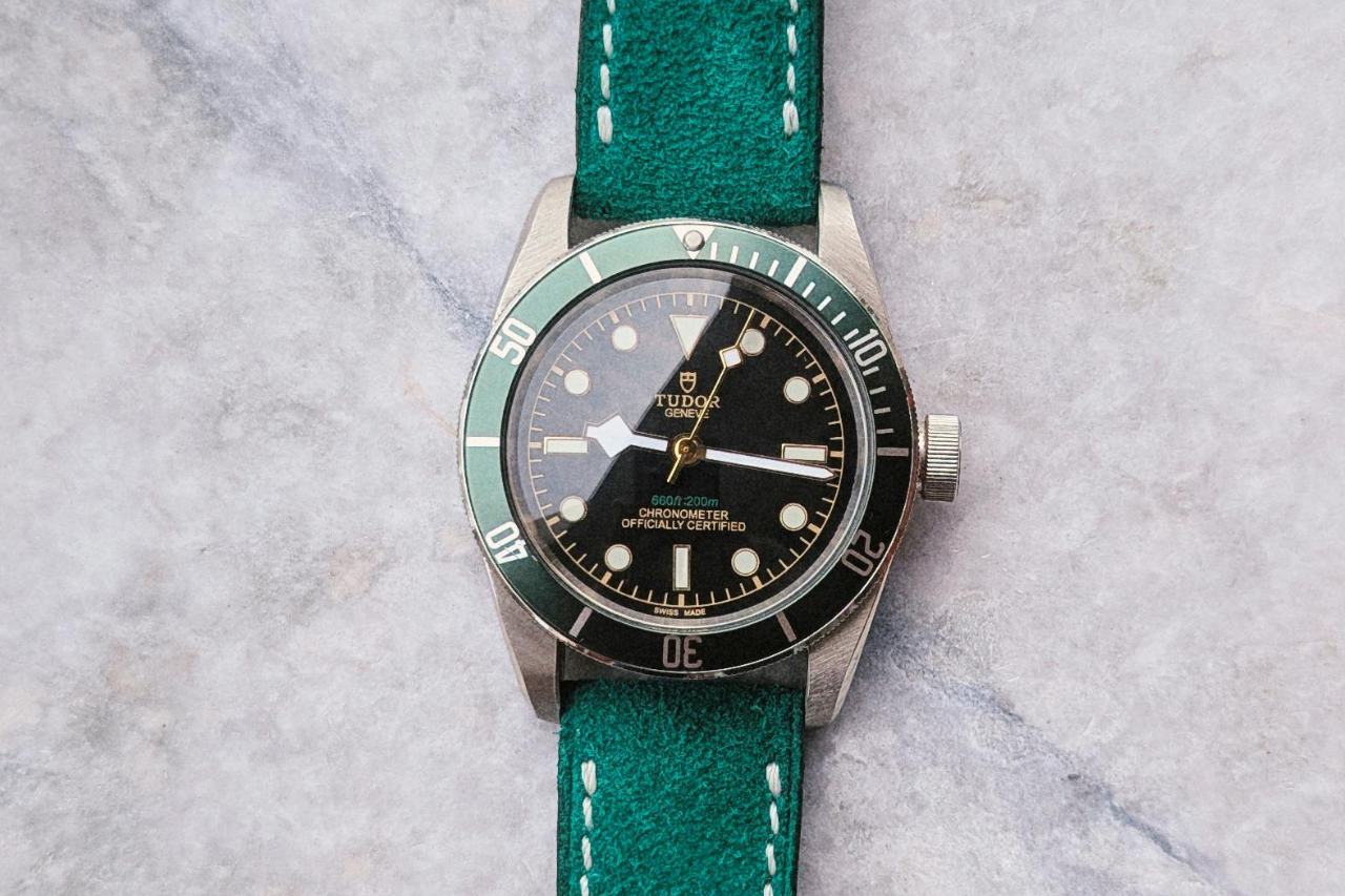 A TUDOR watch with green bezel and bracelet on a marble surface.