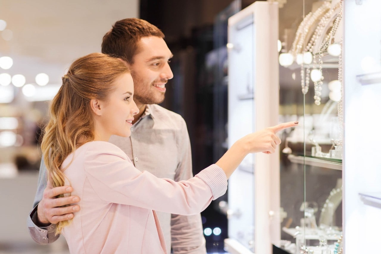 A couple looks at necklaces in a glass case, the woman pointing to one.