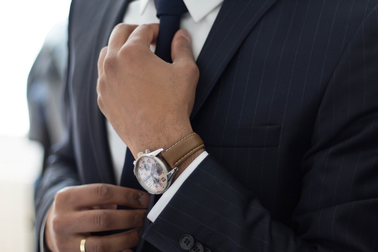 Man, probably a father, adjusting his tie while wearing an elegant watch.