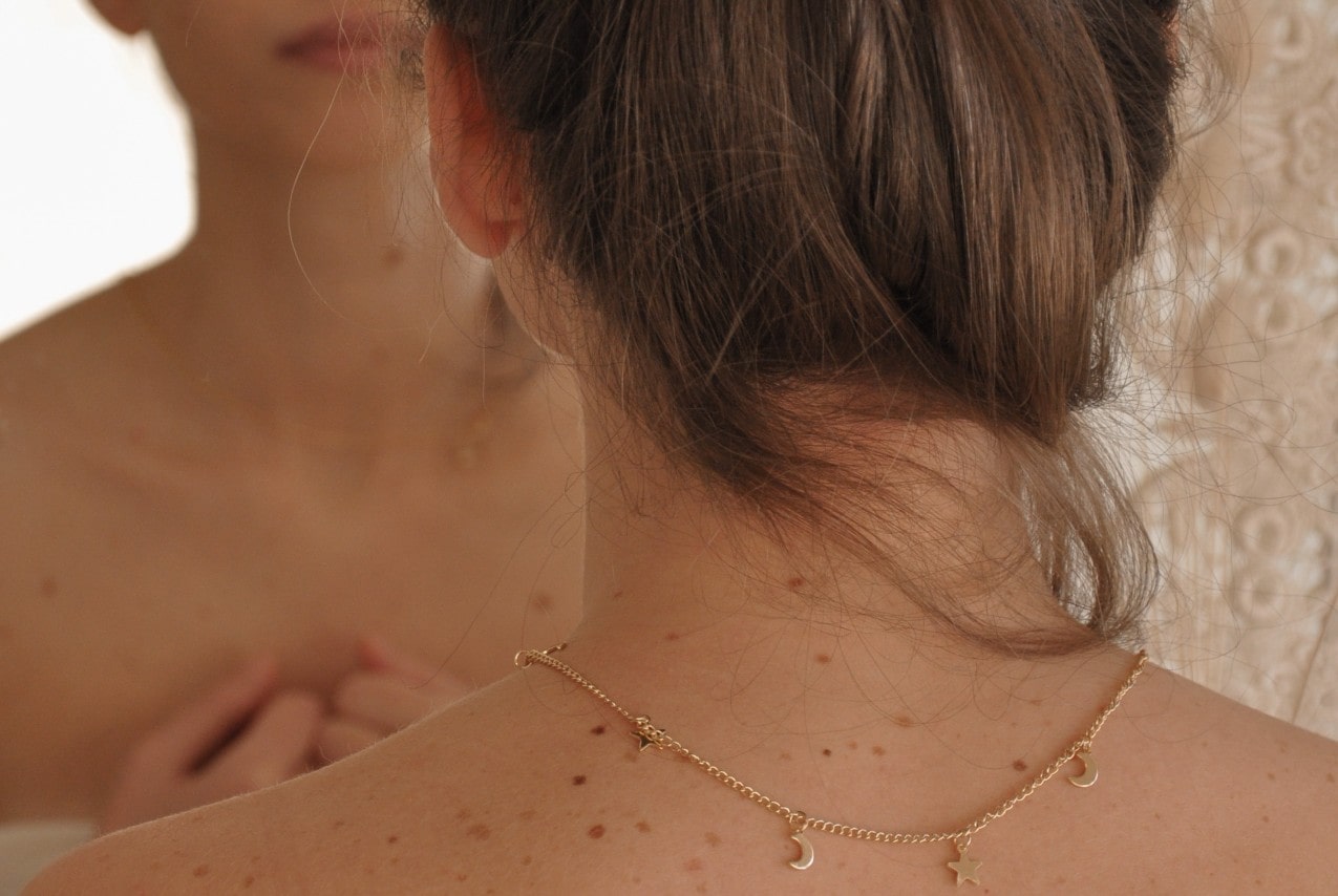a posterior view of a woman wearing a yellow gold necklace with star and moon motifs