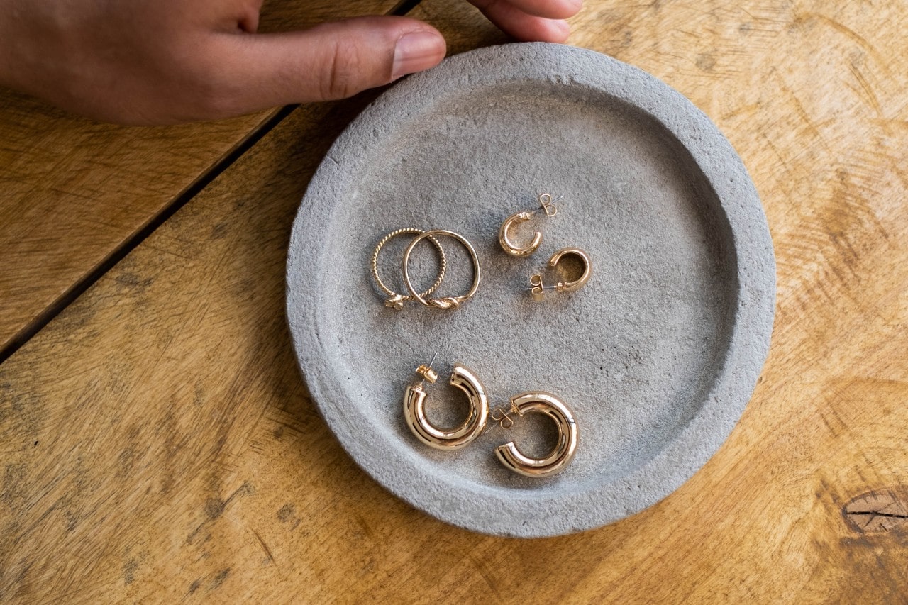 three pairs of small gold huggies earrings in a cement dish