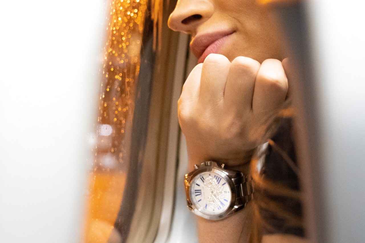 A woman looking out of the airplane window, showcasing her metallic wristwatch with white dial, adorned with diamonds