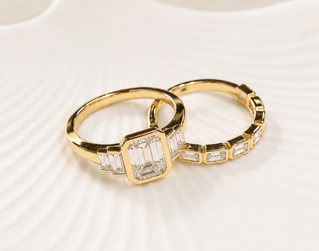 Yellow gold matching bezel engagement ring and wedding band with radiant and emerald cut diamonds sitting in a pale seashell bowl