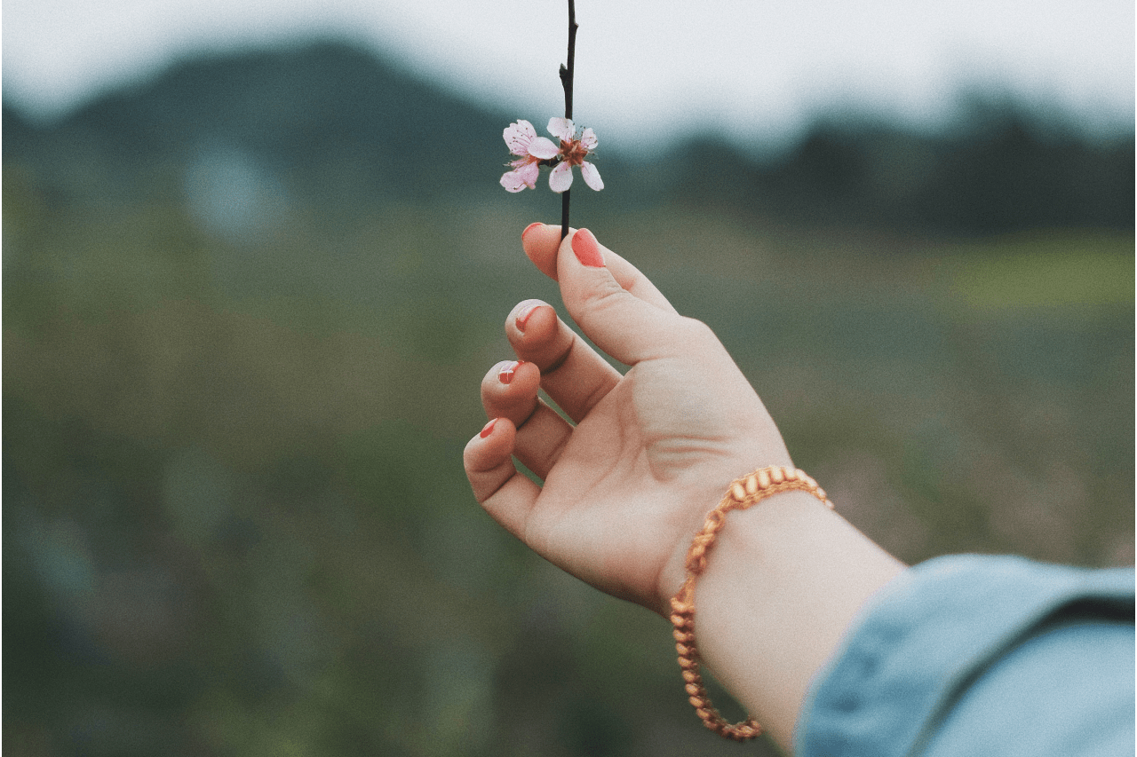 a woman holding a blossom and wearing a copper link bracelet.
