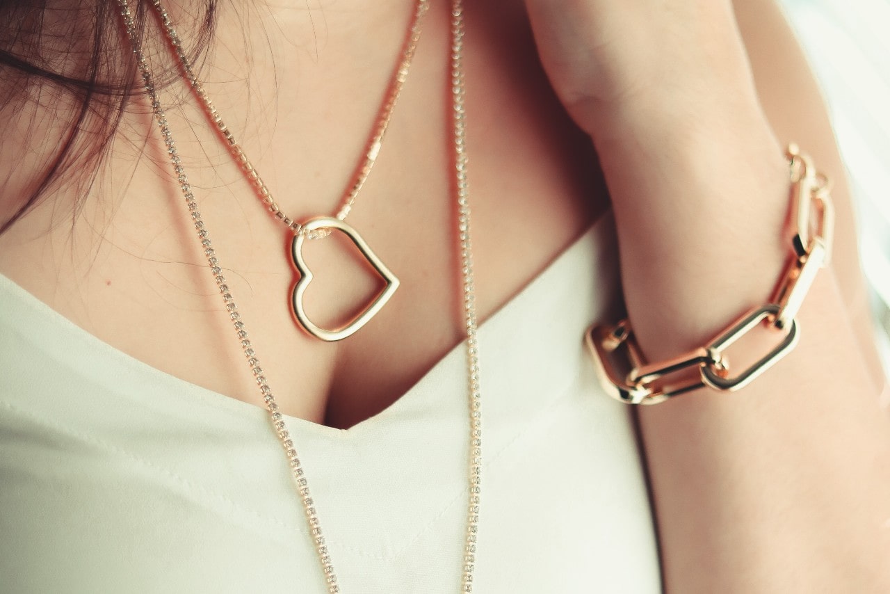 a woman wearing a chunky chain bracelet and a gold heart pendant.