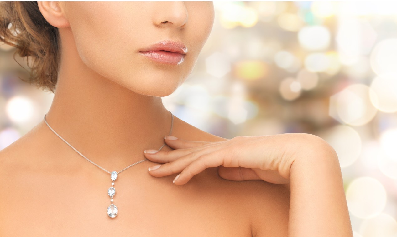 A woman with glossy lips and soft skin wears a delicate necklace with three sparkling pendants.