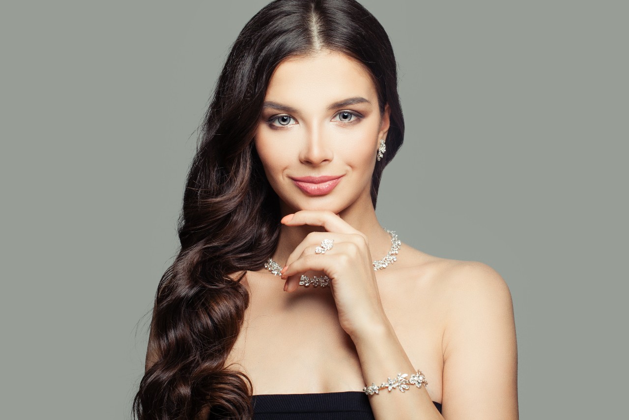 An elegant woman with long, dark hair smiles confidently, wearing a strapless black dress and sparkling jewelry.