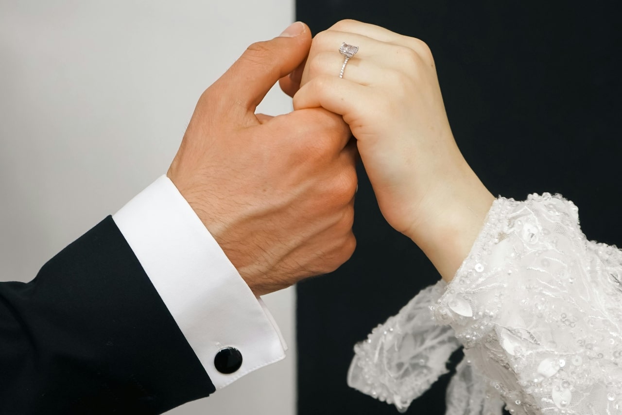 A groom holding a bride’s hand, showcasing a white gold radiant cut diamond engagement ring.
