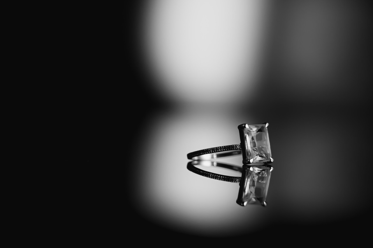 A white gold radiant cut diamond engagement ring on a dark reflective surface.