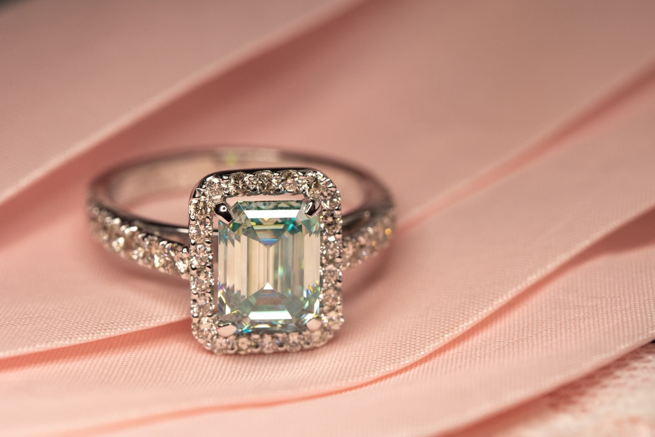 A side stone diamond radiant cut engagement ring on a pink ribbon.