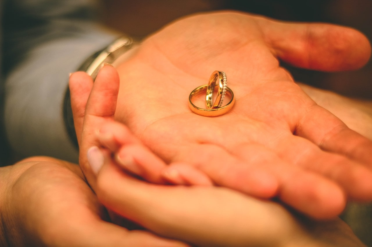 a man’s hand holding two yellow gold wedding bands in his palm