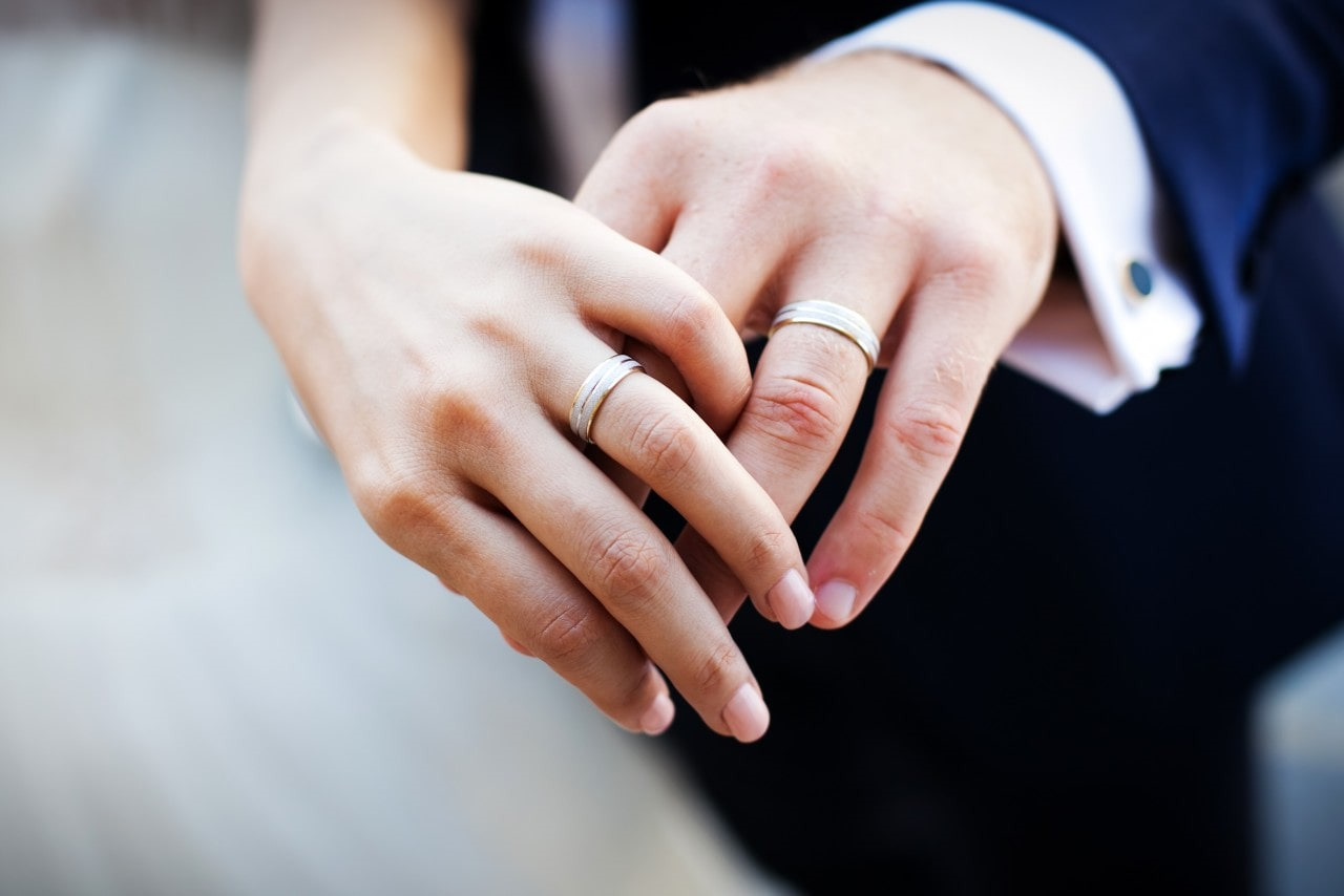 a man and woman’s hands clasped together, wearing matching wedding bands