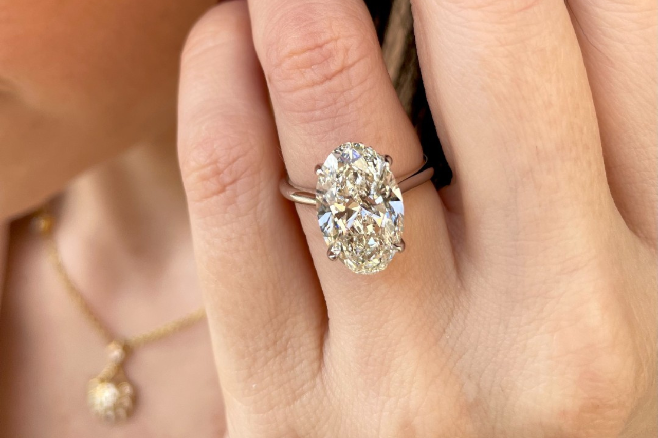 a woman’s hand, donning a white gold marquise cut engagement ring, being held by a man’s hand