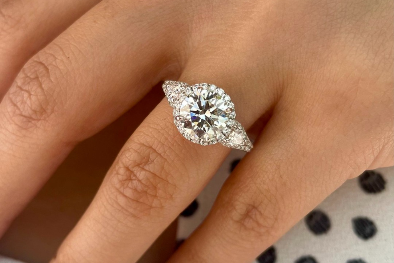 a couple intertwining their pinkies, the woman wearing a white gold halo engagement ring