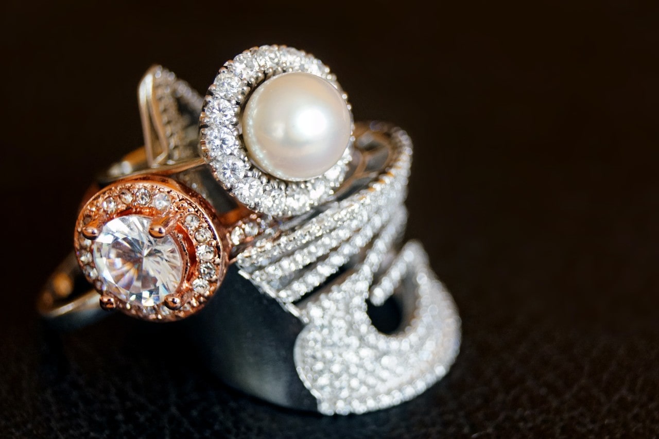 Close-up of luxurious rings featuring a pearl, diamonds, and intricate metalwork on a dark background. Close-up of luxurious rings featuring a pearl, diamonds, and intricate metalwork on a dark background.