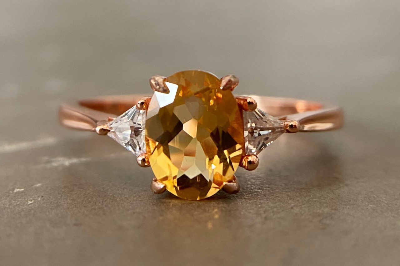 A close-up of a rose gold ring with an oval cut tourmaline center stone. A close-up of a rose gold ring with an oval cut tourmaline center stone.