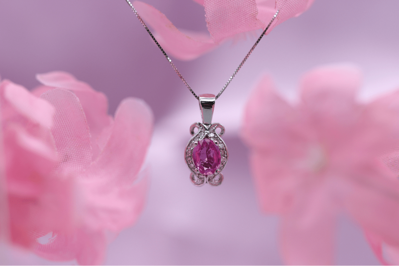 A close-up of a delicate pendant necklace with a distinctive pink center stone. A close-up of a delicate pendant necklace with a distinctive pink center stone.