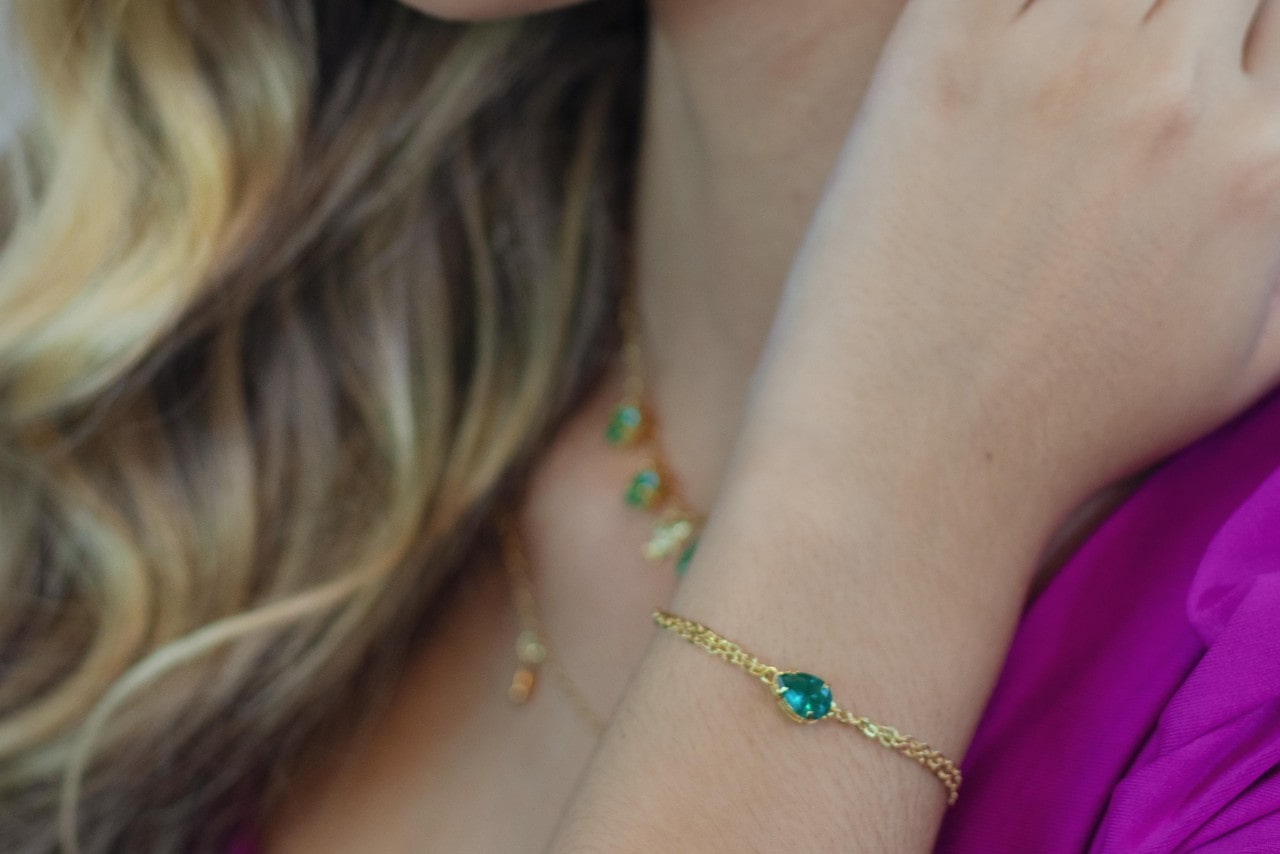 A close-up of a woman wearing a matching necklace and bracelet set featuring teal gemstones. A close-up of a woman wearing a matching necklace and bracelet set featuring teal gemstones.