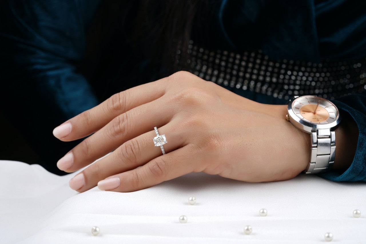 a woman’s hand resting by pearls, wearing a radiant-cut engagement ring and watch.