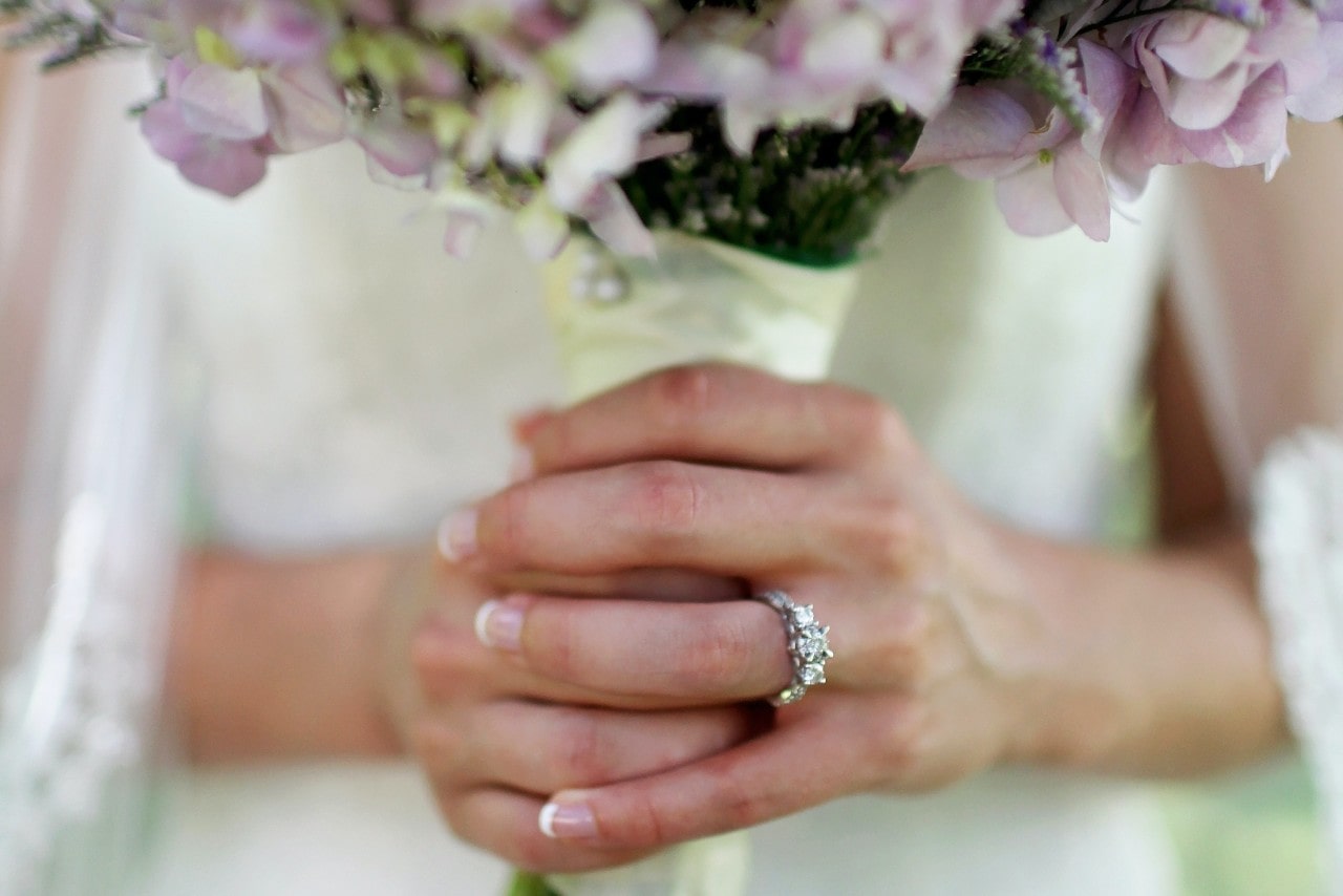 A bride wearing a three stone engagement ring holds her bouquet