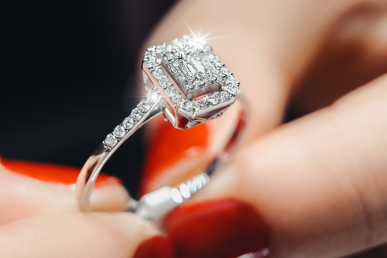 A woman with red nails holds a halo engagement ring.