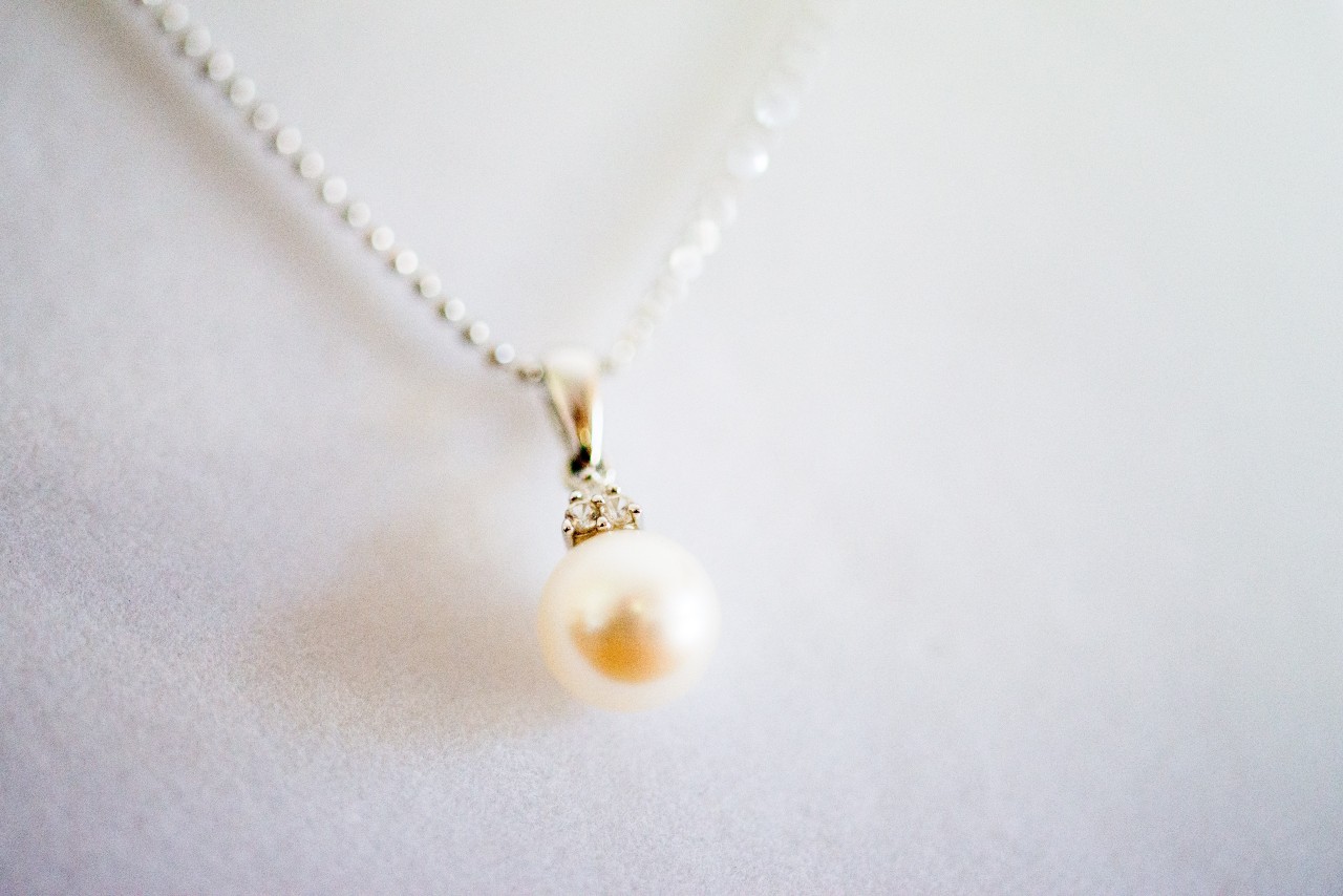 A pearl pendant with a small diamond accent hangs from a fine silver chain against a white background. A pearl pendant with a small diamond accent hangs from a fine silver chain against a white background.