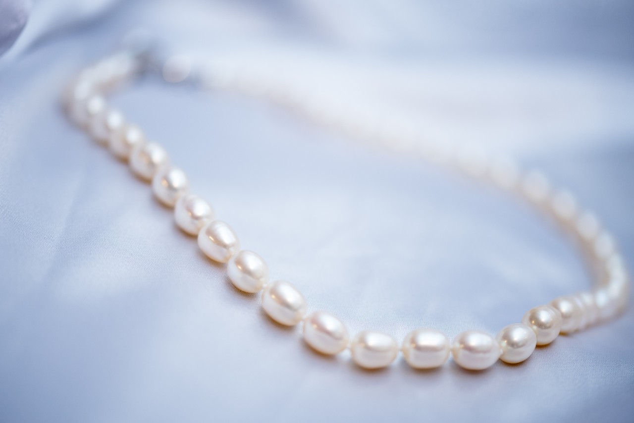 A close-up of a strand of oval-shaped white pearls displayed on soft blue satin. A close-up of a strand of oval-shaped white pearls displayed on soft blue satin.