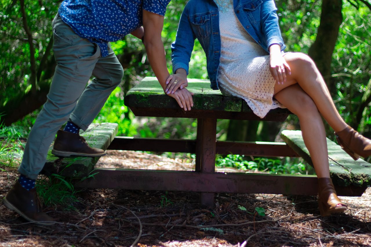 a man and woman holding hands at a picnic table in the woods