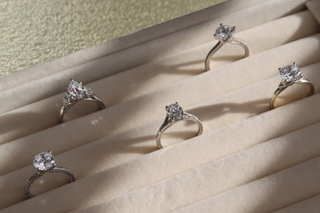 A close-up of an emerald-cut diamond engagement ring with a sleek silver band on a dark surface. A close-up of an emerald-cut diamond engagement ring with a sleek silver band on a dark surface.