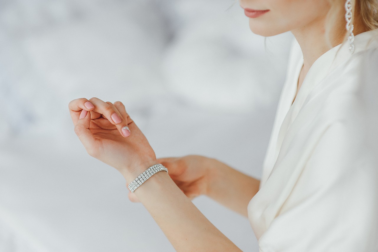 Close-up of a woman in white, adjusting her silver diamond bracelet while wearing sleek silver earrings. Close-up of a woman in white, adjusting her silver diamond bracelet while wearing sleek silver earrings.