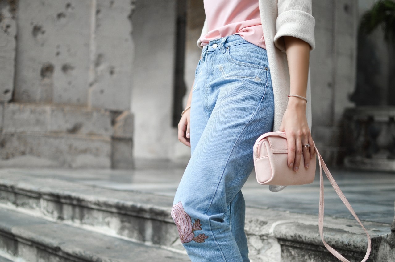 Stylish woman wearing jeans, a pink top, and a light shrug, holding a pink handbag against a neutral setting. Stylish woman wearing jeans, a pink top, and a light shrug, holding a pink handbag against a neutral setting.