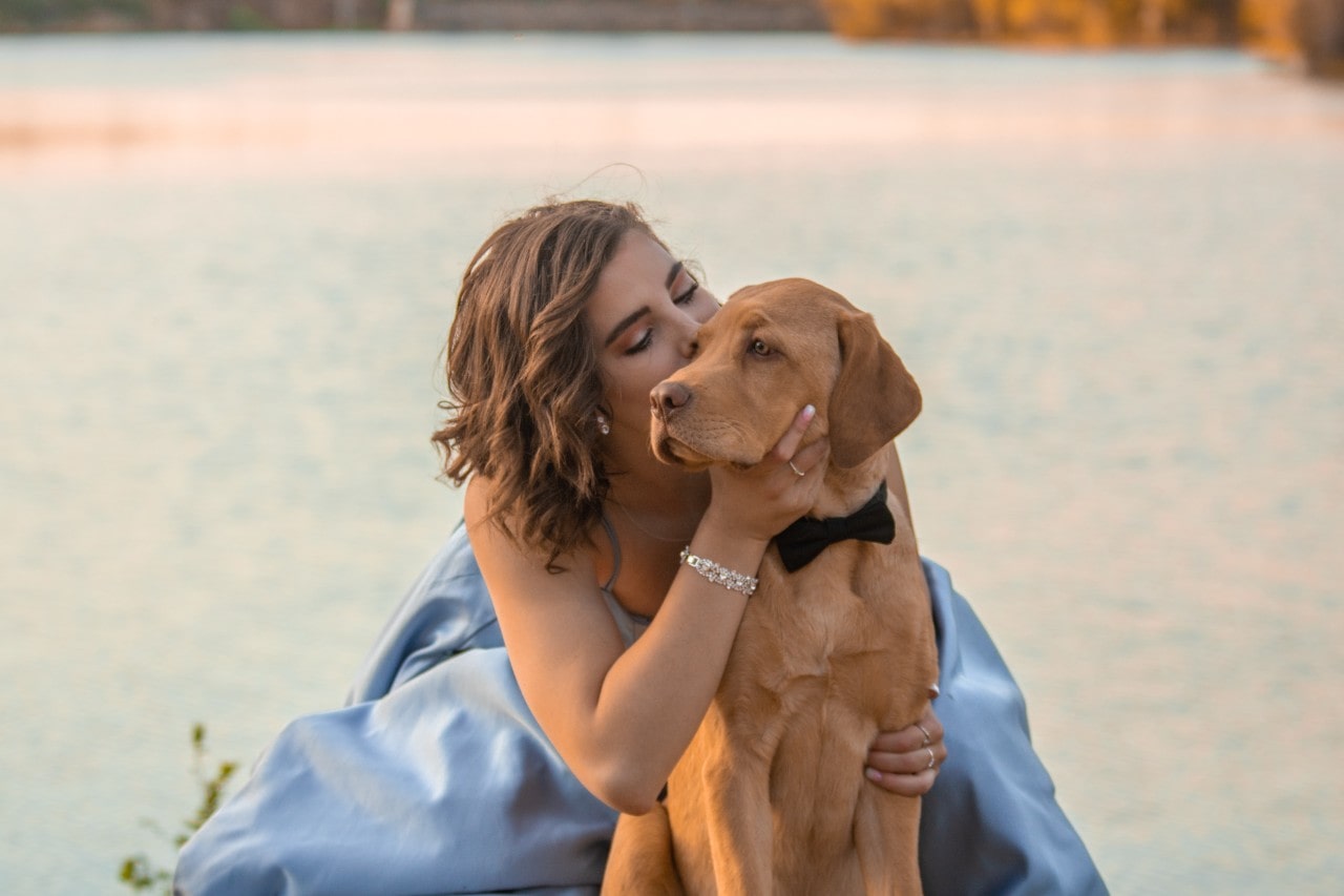 Woman in a flowing blue dress hugs her dog wearing a bow, her silver diamond bracelet catching the light. Woman in a flowing blue dress hugs her dog wearing a bow, her silver diamond bracelet catching the light.