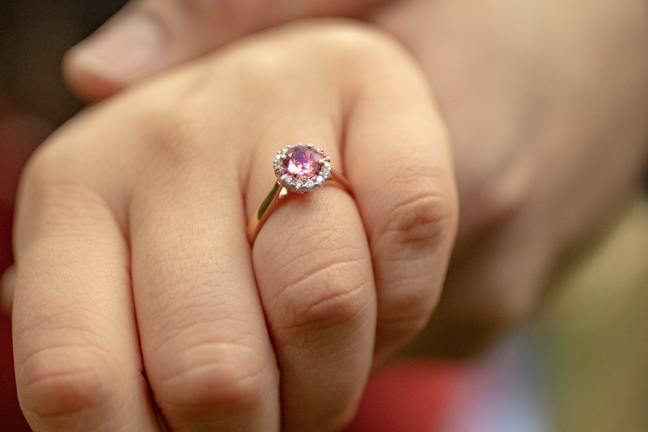 close up image of a hand wearing a rose gold engagement ring and a pink center stone